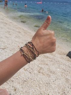 a person's arm with bracelets on the beach and people in the water