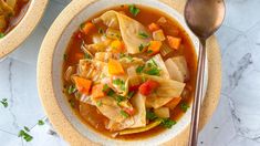 two bowls filled with vegetable soup on top of a table next to silverware and spoons