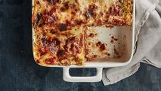 a casserole dish with meat and cheese in it on a white cloth next to a fork