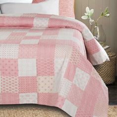 a pink and white quilted bedspread on a bed with flowers in vases