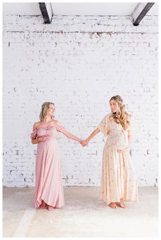 two women holding hands in front of a white brick wall with exposed beams on the ceiling