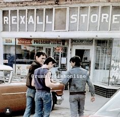 three young men standing in front of a store talking to each other on the sidewalk