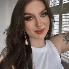 a woman with tattoos and piercings on her face posing for a photo in front of a window