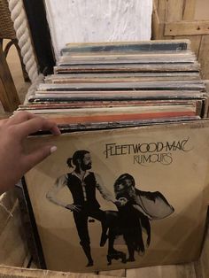 a person holding up a record album in front of a stack of records on a chair