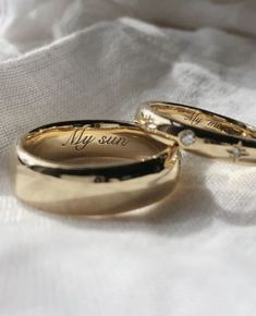 two gold wedding rings with the words my sun written on them sitting on a white cloth