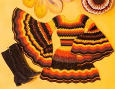 an assortment of crocheted clothing and shoes on a yellow surface with pumpkins