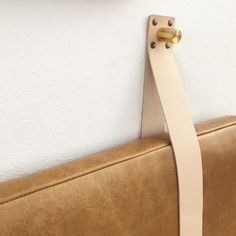 a tan leather couch with a white strip hanging from it's back end and a gold metal hook on the wall