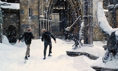 two people are walking through the snow in front of an old building