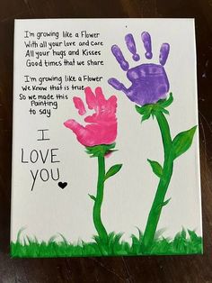 a handprinted card with two pink and purple flowers in the grass that says, i love you