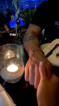 two people holding hands in front of a lit candle at a table with other people