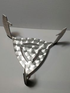 a metal object that looks like an ornament on a white surface with light reflecting off it