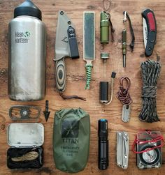 the contents of an outdoor survival kit laid out on a wooden table, including water bottle, knifes and other items