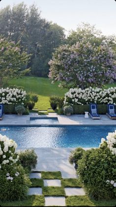 an outdoor swimming pool surrounded by trees and bushes with white flowers in the foreground