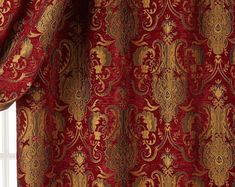 a red and gold curtain hanging in front of a window with an ornate pattern on it