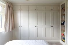 a bed sitting under a window next to a white closet filled with books and toys