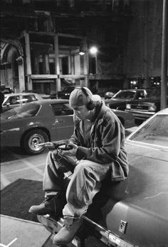 a man sitting on top of a car while looking at his cell phone and listening to headphones