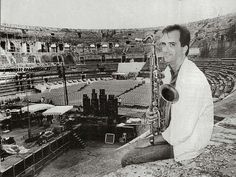 a man sitting on top of a rock next to a saxophone in front of an empty stadium