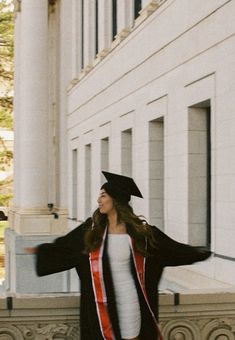 a woman in a graduation gown and cap is walking down the street with her arms outstretched