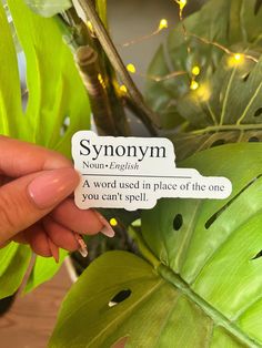 a hand holding a sticker that says, synonym on it next to a plant