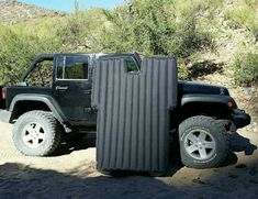 a black jeep with a large piece of luggage strapped to it's back in the desert