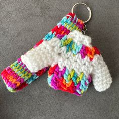 two crocheted mittens sitting on top of a gray carpet next to a pair of scissors