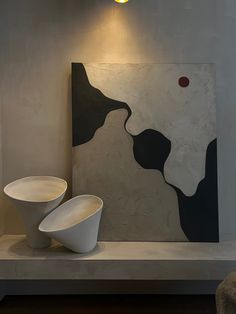 two white bowls are sitting on a table in front of a large abstract painting and light fixture