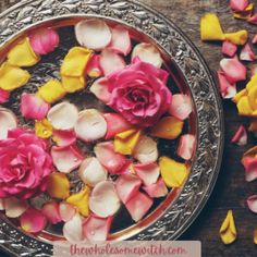 pink and yellow flowers floating in water on top of a metal platter with petals