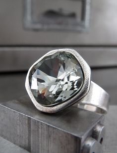 Absolutely stunning crystal ring in Swarovski's classic 'Black Diamond' color -- endlessly sparkling, yet understated + sophisticated. This cushion-cut, timelessly elegant + moody Swarovski crystal is set into a beautiful, high-quality, cast antiqued silver-plated adjustable ring with an modern + minimalist bezel. Black Diamond Swarovski cushion-cut crystal: 12mm dia (1/2") Antiqued silver-plated adjustable ring Adjustable from approx size 6 to 9. May be loose on small fingers.