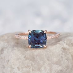 a blue cushion cut diamond ring on top of a rock with diamonds around the band