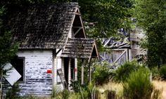 an old run down house sitting in the middle of a field with tall grass and trees