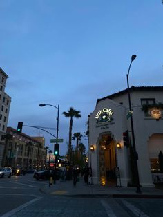 an empty street at dusk with cars parked on the side and palm trees in the background