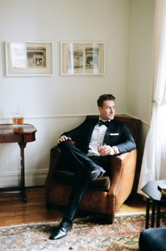 a man in a tuxedo is sitting on a chair and holding a drink