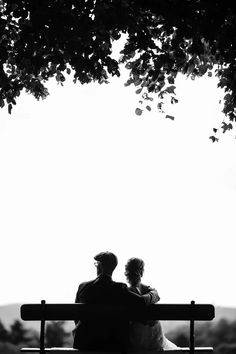 two people sitting on a bench under a tree