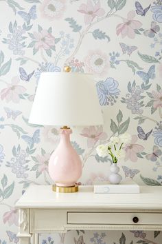 a pink lamp sitting on top of a white table next to a wallpapered wall