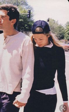 a man and woman are walking down the street holding hands while wearing baseball caps on their heads