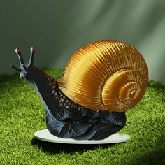 a snail figurine sitting on top of a plate in the grass with it's eyes closed