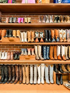 many pairs of boots are lined up on the shelves in front of a brick wall