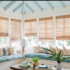 a living room filled with lots of windows covered in blinds and pillows on top of them