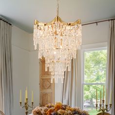 a chandelier hanging over a dining room table with flowers and candles on it