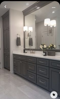 a large bathroom with two sinks and mirrors on the wall, along with gray cabinets