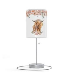 a lamp that has a cow on it with flowers around the base and a white shade