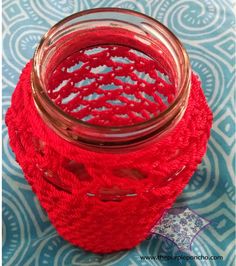 a glass jar filled with red yarn sitting on top of a blue and white table cloth