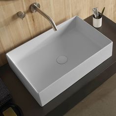 a white square sink sitting on top of a wooden counter next to a toilet paper dispenser