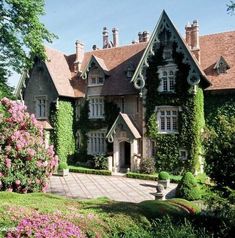 a large house covered in vines and flowers next to a lush green field with pink flowers