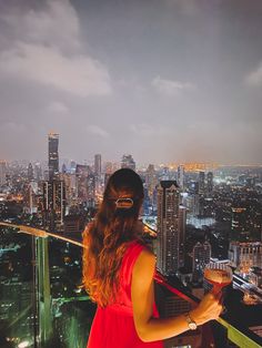 a woman in a red dress standing on top of a building looking at the city