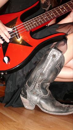 a woman sitting on the floor with her legs crossed and holding a red electric guitar