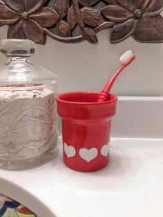 a red cup with a toothbrush in it sitting next to a glass container on a counter