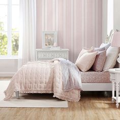 a bedroom with pink and white striped wallpaper, bedding and furniture in it