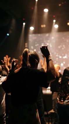 a group of people standing in front of a stage with their hands up to the sky