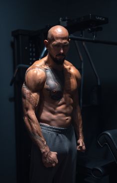 a man with no shirt standing in front of a gym equipment rack and looking at the camera